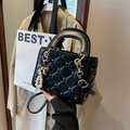 Quilted black handbag with gold star studs and a pearl bow charm on a beige background - Black