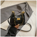 Detail of black quilted suede shoulder bag with gold twist lock and chain strap over a grey blazer - Black