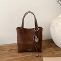 Detail of dark brown suede patchwork handbag with leather tassel on a rustic wooden stand - Coffee with Pendant