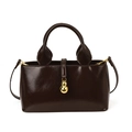 Glossy dark brown bucket bag with gold pendant and leather top handles on white background - Brown