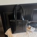 Borsa tote in pelle nera lucida con logo metallico su una scrivania moderna - Nero
