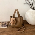 Detail einer braunen Eimer-Tasche aus Leder mit Plüschbären-Anhänger auf Holztisch - Mit Anhänger / Braun