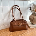 Sac à bandoulière marron aspect daim avec boucle dorée posé sur une table en bois - Brun Foncé