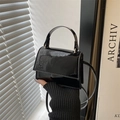 Detalle de un mini bolso de mano en charol negro con asa superior y correa fina - Negro