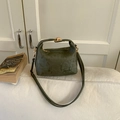 Close-up of dark green leather handbag with golden lock on a white sofa setting - Green