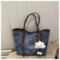 Detail of blue denim tote bag featuring brown leather trim and a white cloud plush charm - Blue with Charm