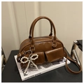 Detailed view of brown patent leather Boston bag with pearl bow charm and dual straps - Brown