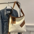 Détail du sac cabas en toile blanche avec bandoulière marron et patch mode sur denim bleu - Blanc