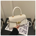 Sac à main blanc avec rabat tissé et boucle M dorée posé sur une chaise noire - Blanc
