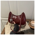 Detalle del bolso de media luna rojo oscuro con acabado brillante y colgante de lazo - Rojo