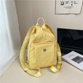 Vibrant yellow nylon backpack with metal logo and front zipper pocket on a desk - Yellow