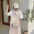 Primer plano de una mochila de lona beige con múltiples bolsillos y cremalleras de color púrpura - Blanco Roto