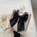 Cream tote bag with large black bow detail and slender shoulder straps in lifestyle setting - White Base Black Bow