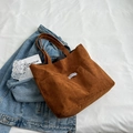 Bolso tote de pana marrón con etiqueta de moda sobre ropa de cama blanca y denim - Marrón