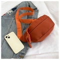 Detail view of orange nylon chest bag with wide woven strap and zipper on white fabric - Orange