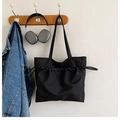 Detalle del bolso tote negro de nailon con diseño de cordón colgado en un perchero - Negro