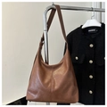 Detail of a brown vintage pleated leather tote bag hanging on a metal rack in a closet - Tan