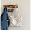 Detalle de bolso tote blanco con cordón colgado junto a auriculares y una chaqueta - Blanco