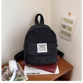 Close-up of black corduroy mini backpack with woven label on a wooden desk setup - Black