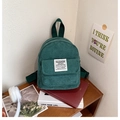 Detail of dark green corduroy mini backpack with fabric label on a wooden shelf - Green
