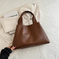 Bolso tote trenzado minimalista en marrón oscuro de cuero sobre fondo de tela blanca - Marrón