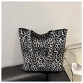 Detail of large leopard print canvas tote bag placed on a black leather sofa with accessories - Black
