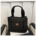 Gros plan du sac cabas en tweed noir et doré avec écusson logo en cuir sur une chaise - Noir