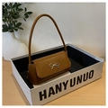 Détail d'un sac baguette en cuir caramel avec boucle métallique en forme de nœud doré - Marron