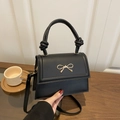 Classic black leather handbag with golden bow detail and knotted handle in a cozy setting - Black