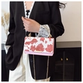 Pink cow pattern crossbody bag with gold handle held by model in casual chic outfit - Pink