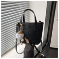 Detail of black PU bucket bag featuring embossed lettering and a white plush toy charm - With Pendant / Black