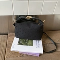 Detalle de bolso vintage de tela negra texturizada con cierre dorado sobre libros - Negro