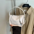 Minimalist cream crossbody bag with silver chain and metal ball detail shown handheld - White