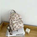 Detail eines Mini-Rucksacks mit Blumenmuster, Gold-Reißverschlüssen auf Buch und Holzregal - Khaki