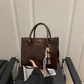 Sac cabas marron en similicuir avec logo doré et chaîne pendentif sur chaise - Marron