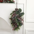 Guirlande de Noël en goutte avec pommes de pin, baies rouges et eucalyptus sur mur blanc - Style Pomme de Pin et Baie Rouge
