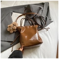 Detail of brown leather bucket bag with chain strap and cute bear charm on white sheet - With Pendant / Brown