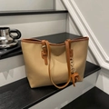 Detail of a large beige tote bag with brown trim and elephant charm on a staircase - Khaki