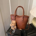 Bolso tote marrón de cuero con colgante de osito y herrajes dorados en luz cálida - Con Colgante / Marrón