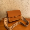 Detalle de bolso bandolera bicolor con correa ancha de jacquard sobre mesa de madera - Marrón