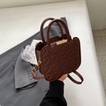Borsa a mano trapuntata marrone con motivo a rombi e finiture dorate su abito grigio - caffè