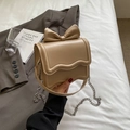 Beige small square bag with large bow and wave edge detail shown in lifestyle setting - Khaki