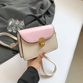 Bolso bandolera rosa y beige con cierre redondo dorado y asa negra sostenido en la mano - Rosa