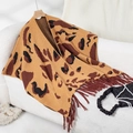 Detail of leopard print knitted poncho with tassel trim draped over a soft sofa - Letter F / Camel