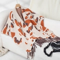 Close-up of knit poncho with bold orange leopard print and dark grey tassel details - Letter F / Apricot