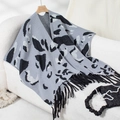 Detailed view of leopard print knit poncho with black fringe trim on a soft base - Letter F / Gray