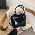 Glänzende schwarze Beuteltasche mit Knotengriffen und Riemen auf einem hellen Blazer - Schwarz
