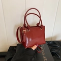 Glänzende dunkelrote Beuteltasche mit dekorativen Knotengriffen und goldener Hardware - Rot