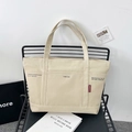 Off-white canvas tote bag with front pocket and black industrial print on a chair - Khaki
