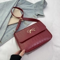 Chique bordeauxrode schoudertas met krokodillenprint en gouden strik op een denim decor - Rood